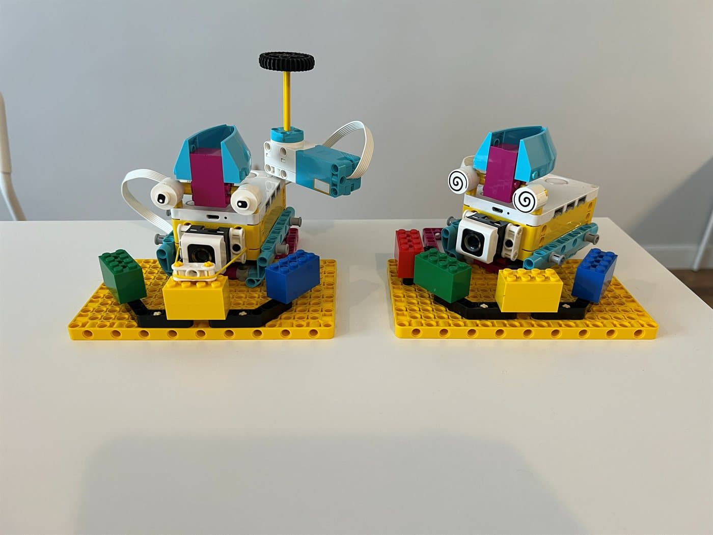 Dwa roboty zbudowane z zestawu LEGO® SPIKE Prime, ustawione obok siebie na żółtych płytkach