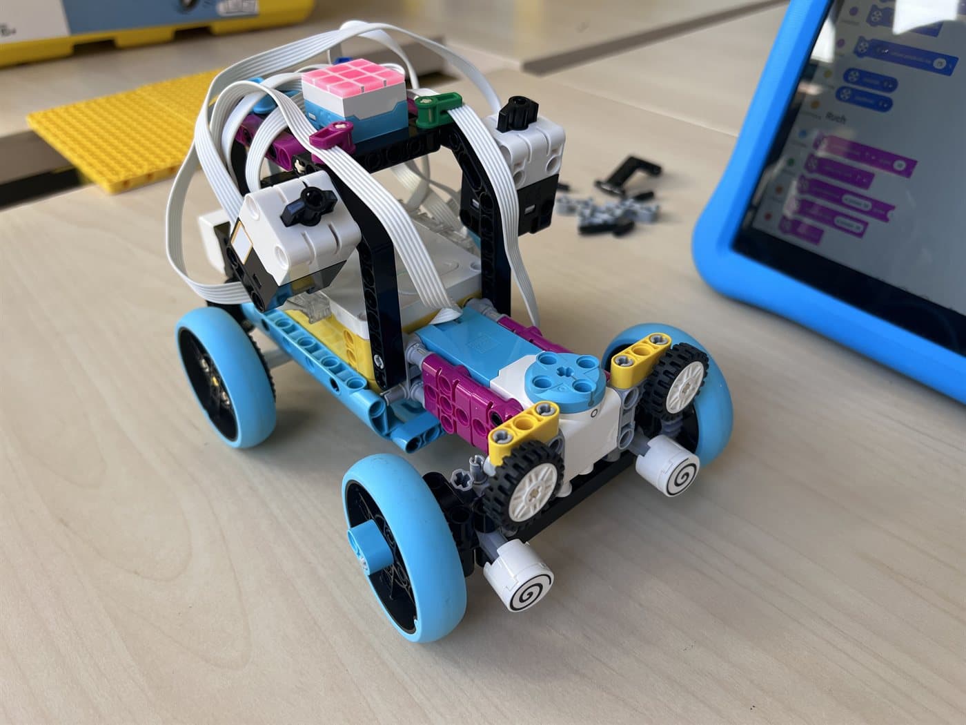 Robot zbudowany z zestawu LEGO® Education SPIKE Prime obok tabletu z programem ułożonym z kolorowych bloków
