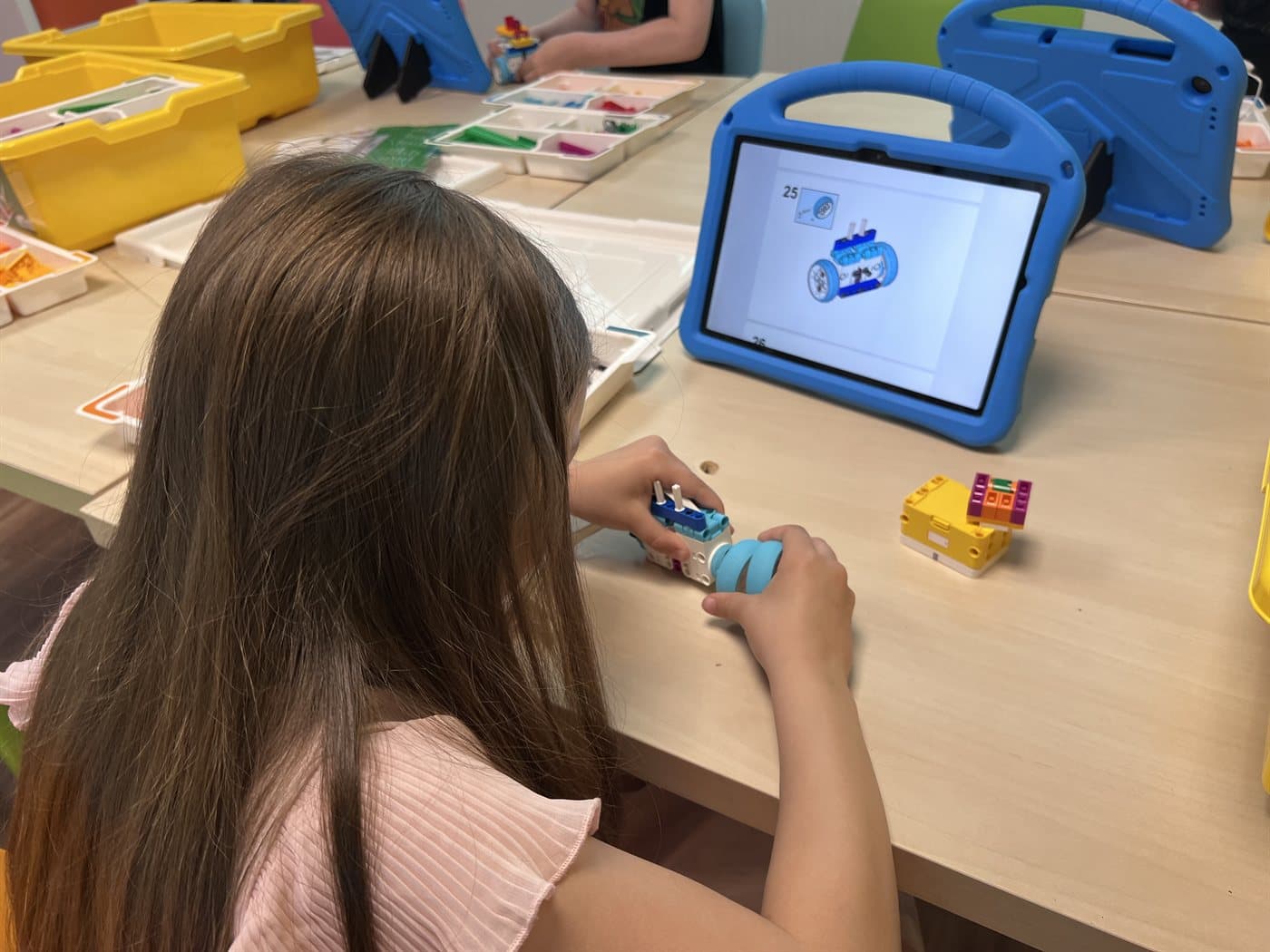 Dziecko składa model z klocków LEGO® Education SPIKE Essential, korzystając z instrukcji na tablecie